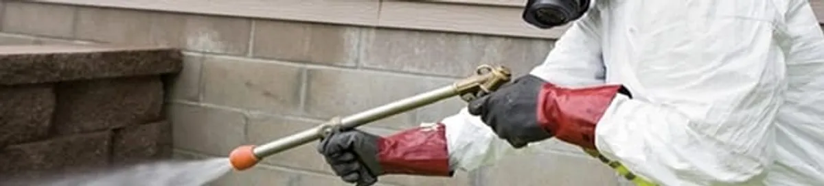 Pest control technician applying exterior insect treatment along a home foundation in Stockton, CA
