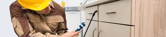 Roach exterminator applying treatment under kitchen cabinets in Stockton, CA