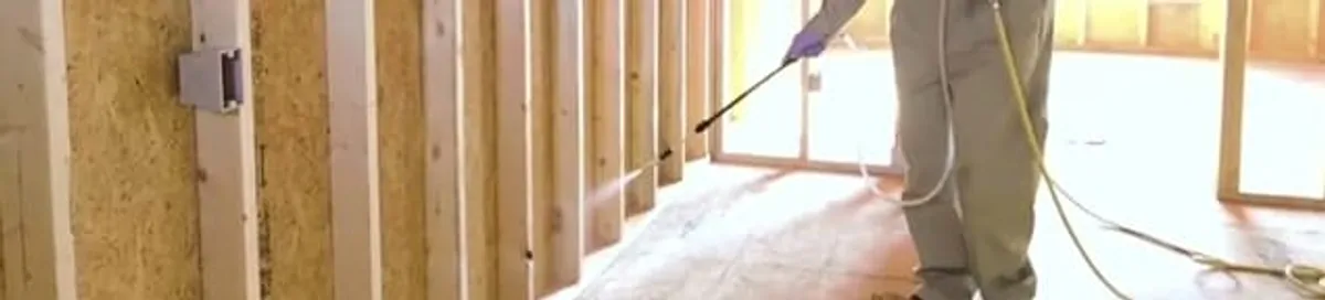 Termite treatment technician applying spray along framing and unfinished walls in Stockton, CA