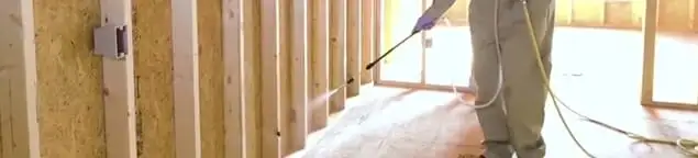 Termite treatment technician applying spray along framing and unfinished walls in Stockton, CA